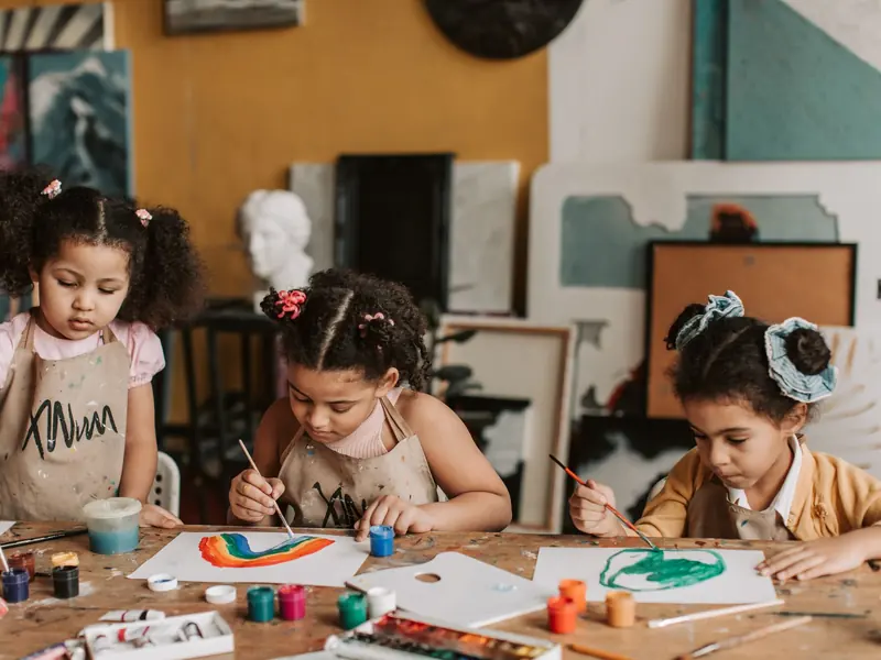 A child painting at an easel in the art room, hands covered in paint.