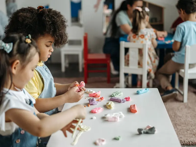Two children in the Early Years room shaping coloured modelling clay at a low table.