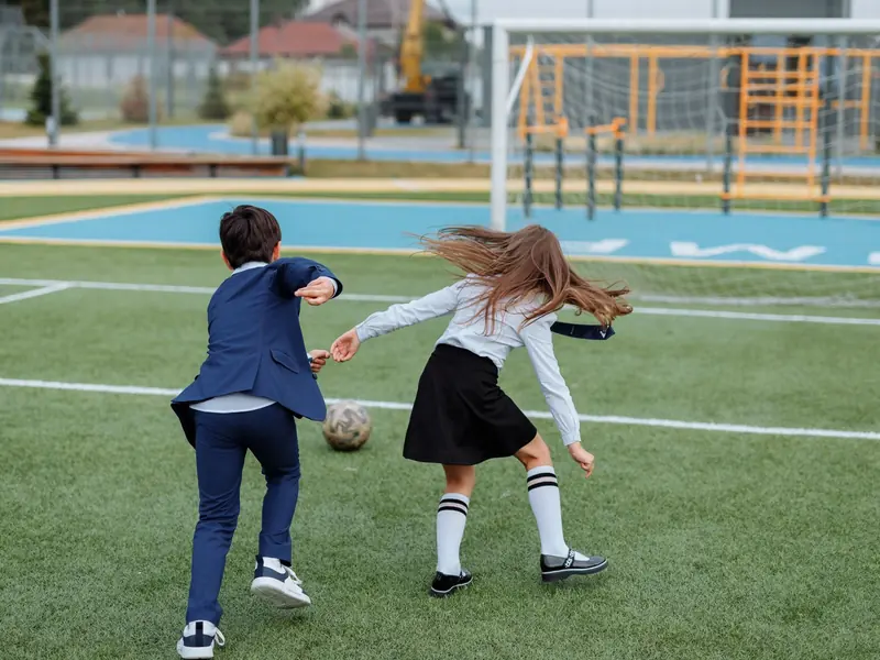 Children running after a football on the school field.