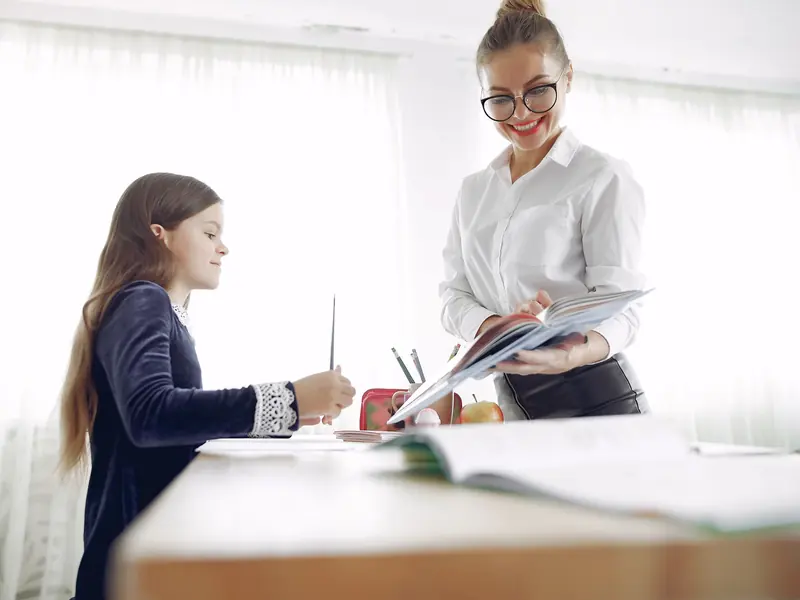 A teacher kneeling beside a desk, going through a piece of work with one child.