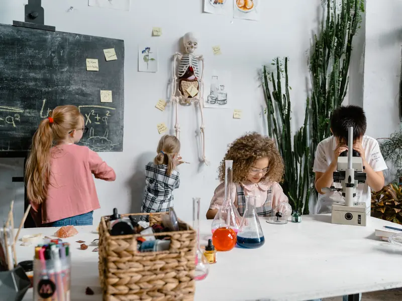 Upper Primary children at the science bench, one at a microscope and one with conical flasks, a skeleton and a blackboard behind them.